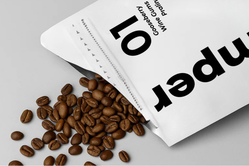 Open coffee bag with coffee beans spilling out on a gray background
